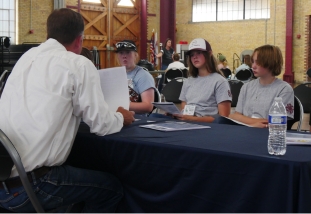 three young people sit at a table facing an adult across the table