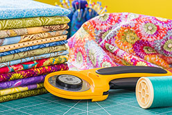 a rotary cutter, thread and colorful fabric