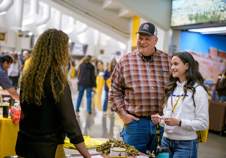 Incoming student standing with her father at New Student Day in the AA at a booth speaking with a UW representative