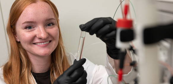 A UW graduate student smiles as they hold a test tube in a University of Wyoming lab.