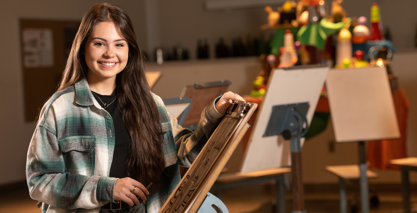 A University of Wyoming student smiles and stands amid several easels.
