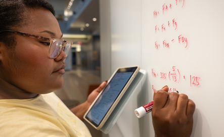 A UW student holds a tablet as they write mathematical equations on a white board at the University of Wyoming.
