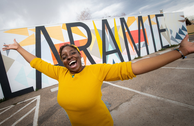 an international student stand in front of a laramie mural