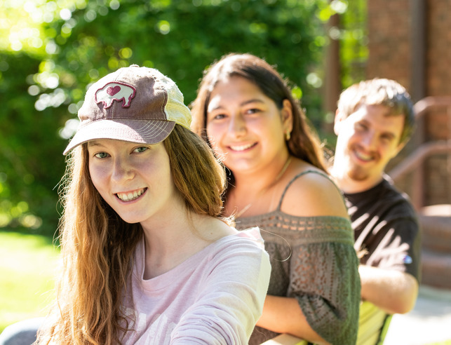 Three students smiling, sitting on bench