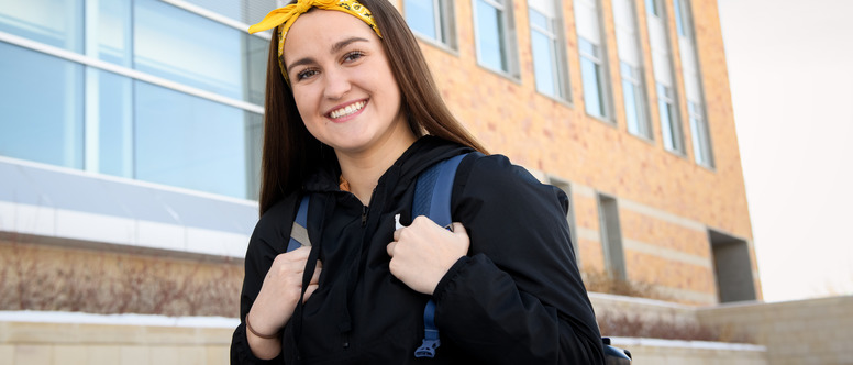 A student outside the engineering building smiling with a backpack on 