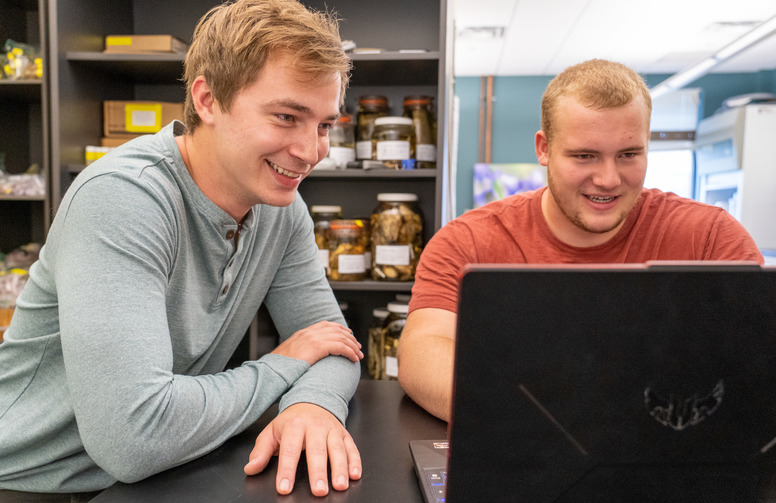 Two students smile and work on a laptop together.