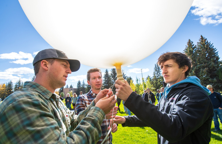 Three students work on a white weather balloon.
