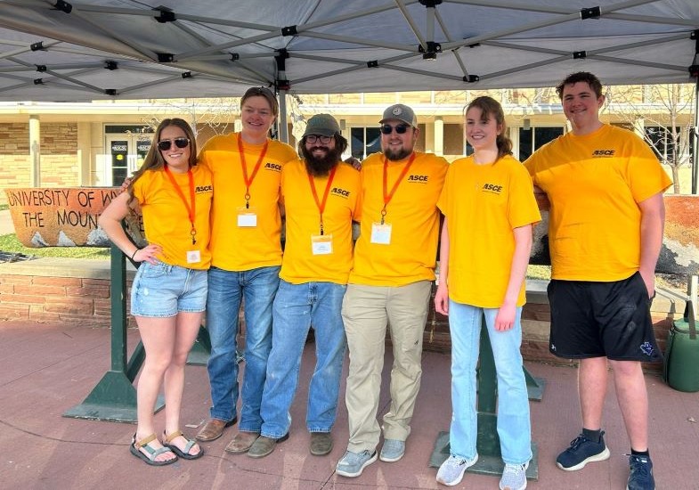 a team of students stand together outside under a tent
