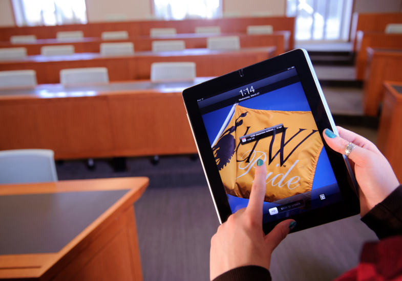 student holding up an ipad with a UW flag in a class room