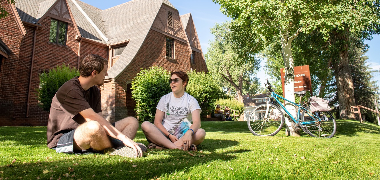 A red-brick, historic house called the Guthrie House featuring a front lawn and trees with students sitting on the lawn.