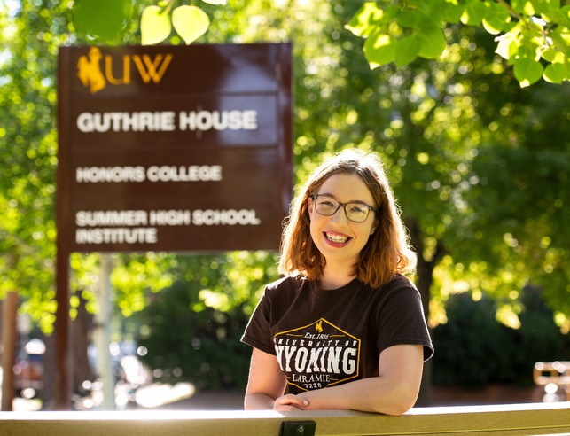Student in a brown shirt in front of the Guthrie House sign