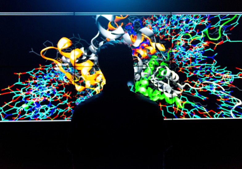 A person stands in front of a colorful screen in a darkened room.