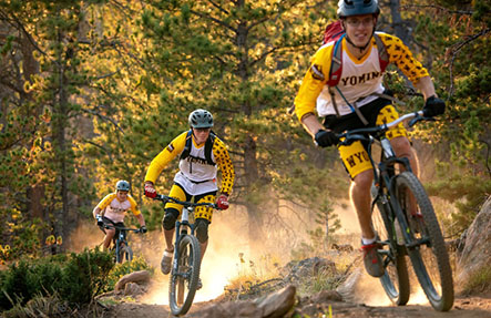 Three men mountain biking Steamboat bucking horse statue by arena auditorium