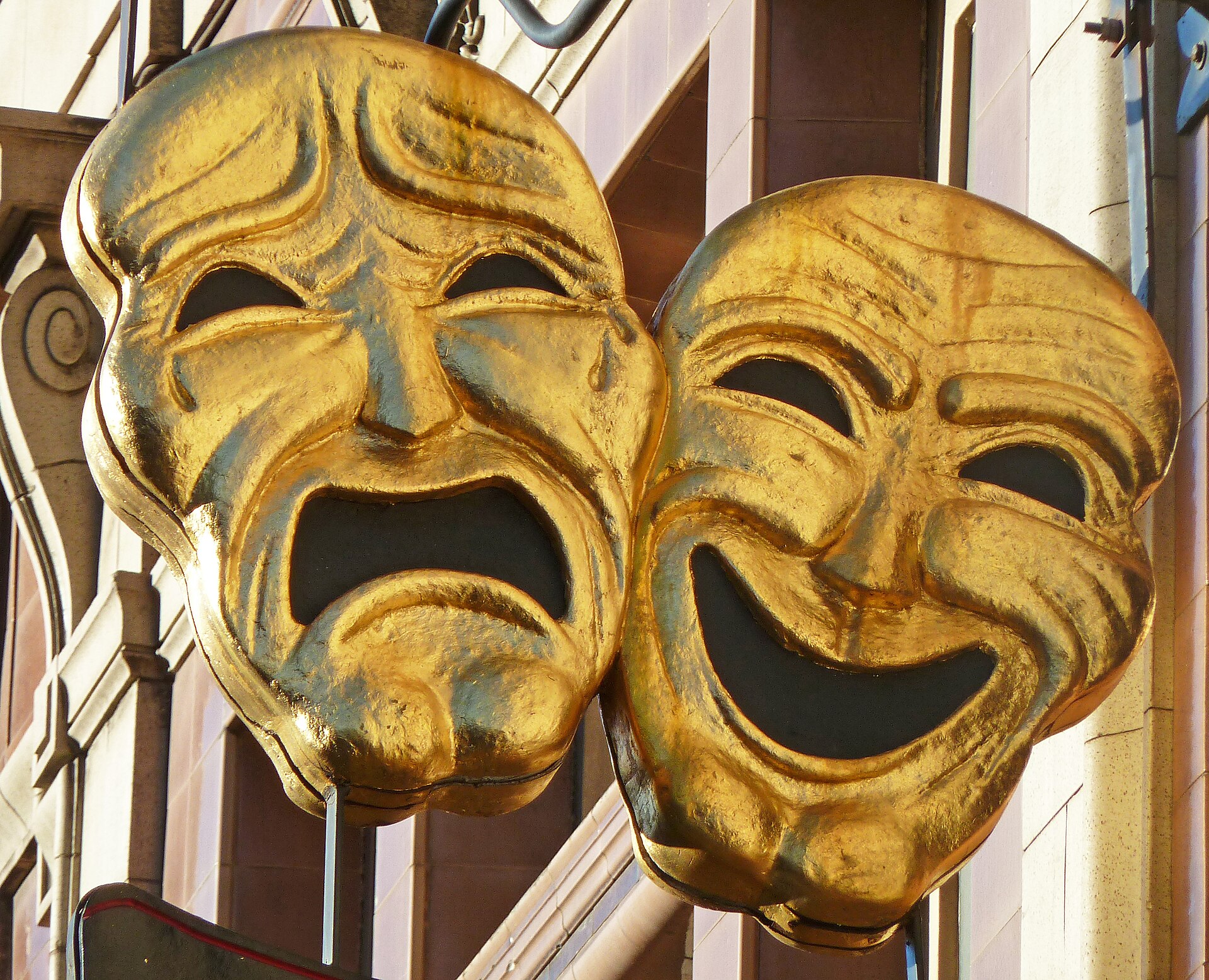 Two large weathered gold theater masks—one frowning and one smiling—mounted on a building facade.