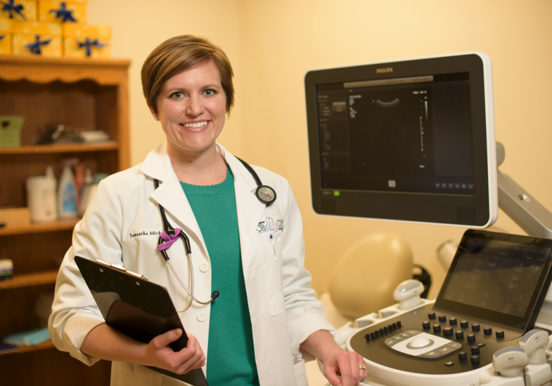 Doctor standing next to a screen and smilling at camera.