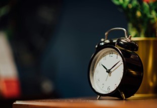 A black analog clock on a night stand.