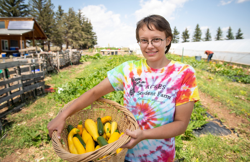 A student at UW stands with a basket of squash smiling at the camera.