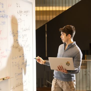 candid photo of an ME student working an equation on a whiteboard in the EERB Collaborative learning space