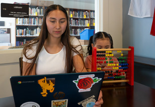 Native American student studying with her daughter playing on an abicus