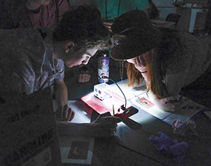 two people leaning over a lit work surface in a dark room