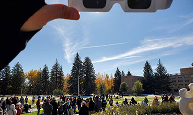 hand holding eclipse view glasses at the top of the photo with crowds at the bottom