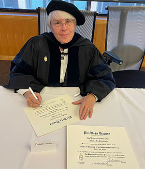 woman in formal academic robes signing certificates