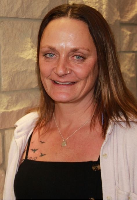 jill proctor wearing a black blouse with a white sweater standing in front of a lime stone wall