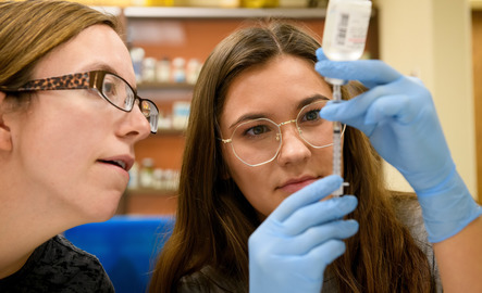Two UW students work together as they use a syringe to pull liquid from a vial in a University of Wyoming lab.