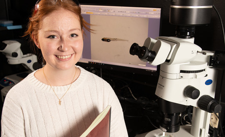 Student stands by a microscope