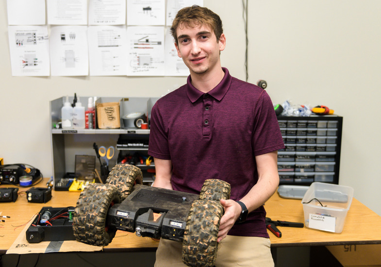 A student smiles for a picture with a robot
