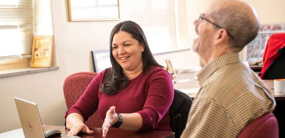 UW staff members work together at a computer, as one laughs and the other controls the laptop