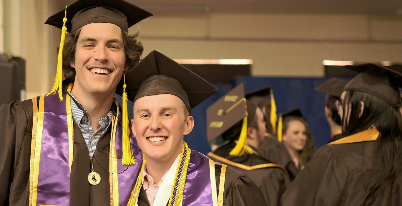 Two UW graduates smile at a University of Wyoming graduation ceremony.