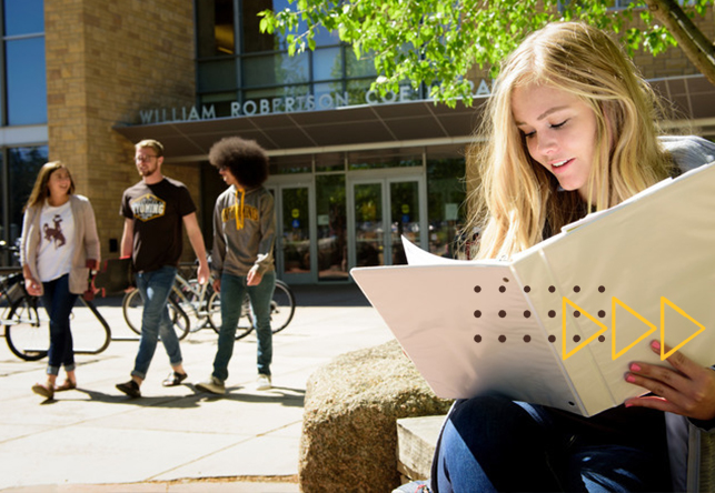 Student looking in binder and three students walking in the background
