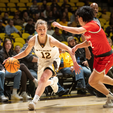 A basketball player on the University of Wyoming's Women's Basketball Team dribbles the ball past a defender