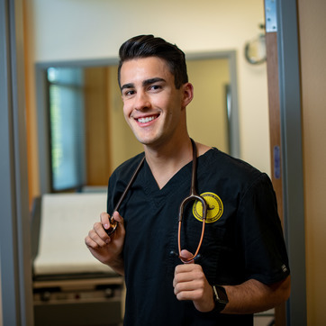 A nursing student smiles for a photo in their scrubs