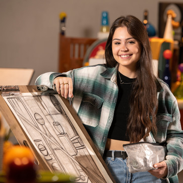 A student smiles with their drawing in an art studio on campus