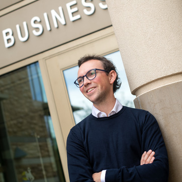 A student smiles off into the distance for a photo in front of the College of Business