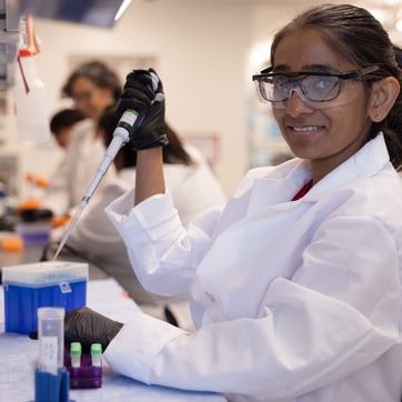 A student researcher smiles for a photo while in a lab