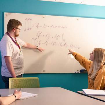 Two students studying a math equation on a white board