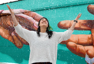 A UW community member stands in front of a mural and broadly smiles as it snows.