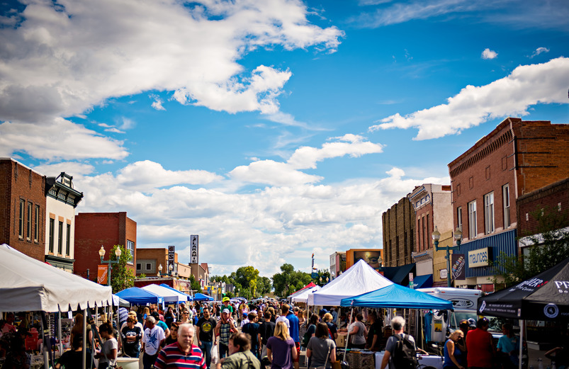 a blue sky above downtown Laramie where a crowd of people are enjoying a farmer's market