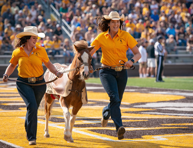 students run across the end zone with cowboy joe during a UW football game