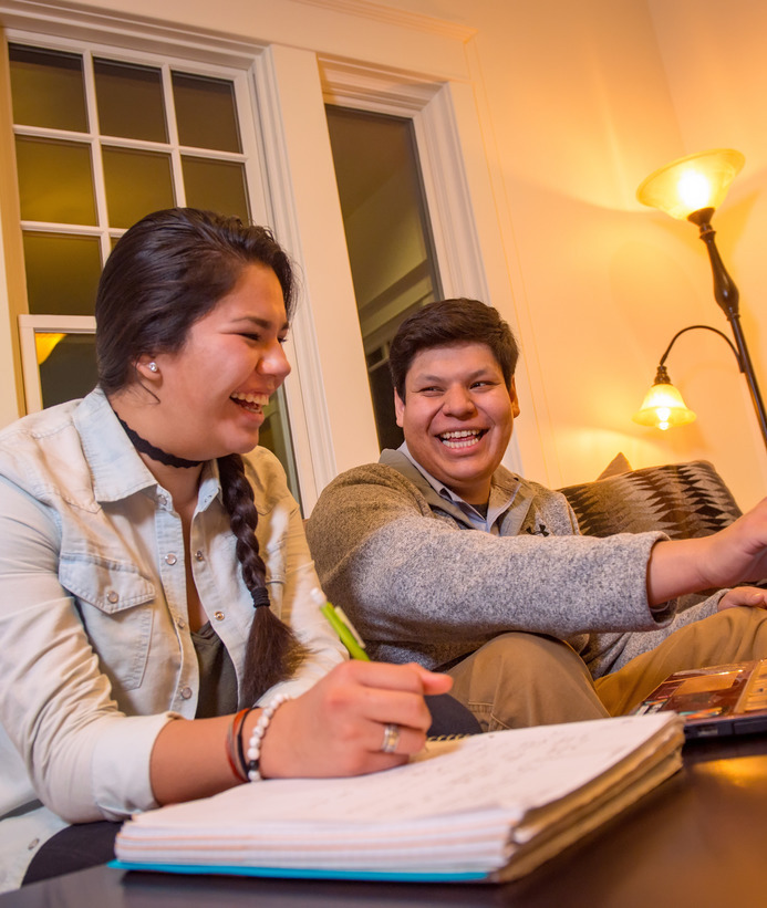 Two students laugh while studying together on a couch