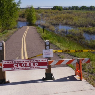 a closed sign blocks a bike path that is flooded beyond the sign