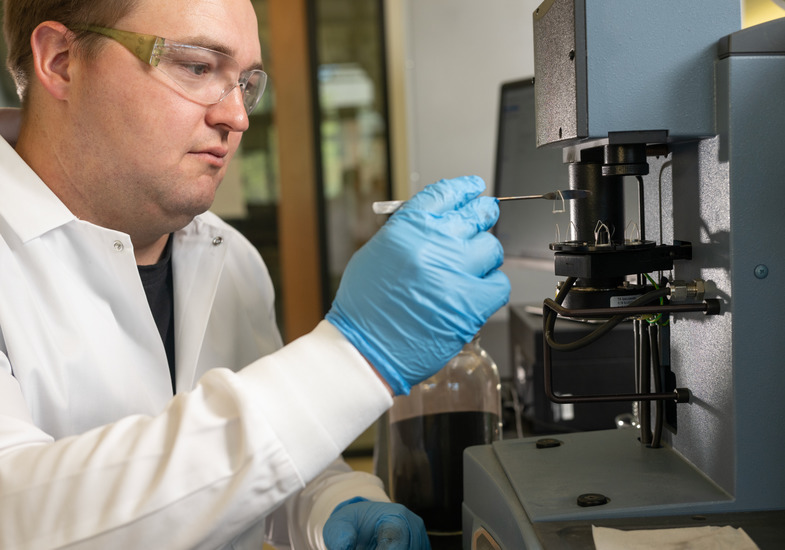 A UW graduate student in a lab coat works with mechanical engineering equipment in a University of Wyoming lab.
