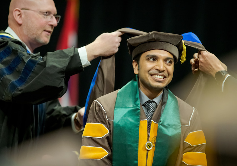 A UW graduate student smiles broadly as they receive their honors during a University of Wyoming commencement ceremony.