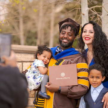 A recent UW doctoral graduate and their family pose in front of a University of Wyoming sign.