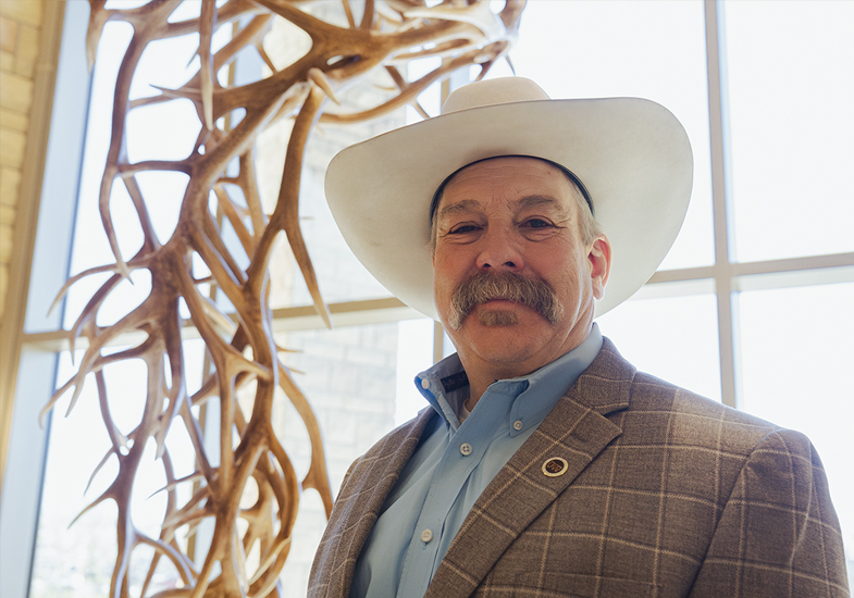 man in a cowboy hat stands in front of a window by a sculpture