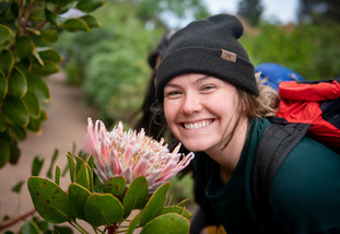 A UW study abroad student smiles broadly next to a flower on an outdoor trek.