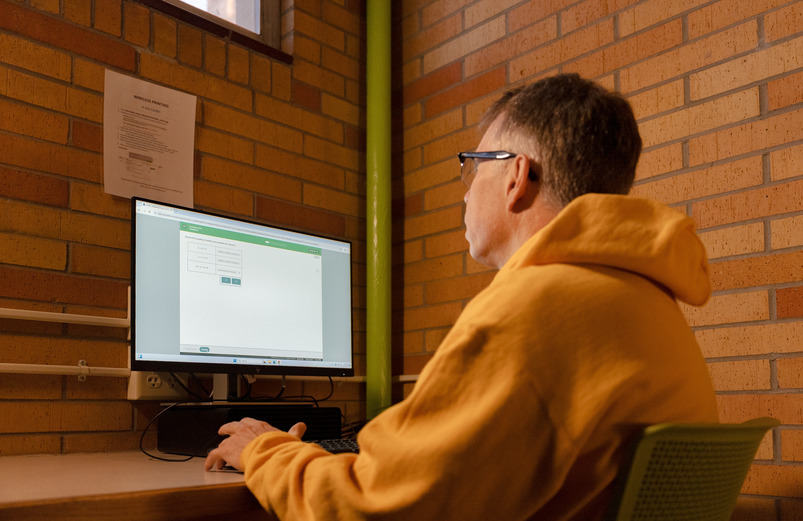 A person sits facing way at a computer.